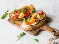 Pair of grilled toasts with cream cheese and slices of fresh tomatoes of various colors with fresh arugula and ground black pepper