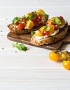 Pair of grilled toasts with cream cheese and slices of fresh tomatoes of various colors with fresh arugula and ground black pepper