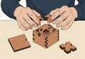 A pair of hands assembles a wooden puzzle cube on a flat surface. Royalty Free Stock Photo