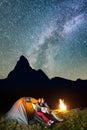 Pair hikers sitting near glowing tent and campfire, looking to the shines starry sky in the camping at night Royalty Free Stock Photo