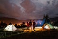 Pair holding hands and their friend stands near campfire