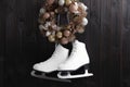 Pair of ice skates and beautiful Christmas wreath hanging on dark wooden wall Royalty Free Stock Photo