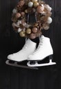 Pair of ice skates and beautiful Christmas wreath hanging on dark wooden wall Royalty Free Stock Photo