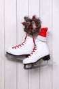 Pair of ice skates with Santa hat and Christmas wreath hanging on white wooden wall Royalty Free Stock Photo