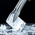 A pair of ice tongs gripping a translucent ice block