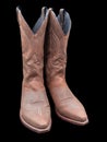 A pair of isolated light brown cowboy boots with stiched patterns against completely black background seen from the front Royalty Free Stock Photo