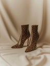 Pair of leopard high heel ankle boots on the backdrop of cream fabric.