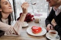 A pair of lovers, a man and a woman, eat with spoons a red heart-shaped dessert in a cafe. Royalty Free Stock Photo