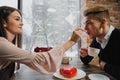 A pair of lovers, a man and a woman, eat with spoons a red heart-shaped dessert in a cafe. Royalty Free Stock Photo