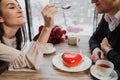 A pair of lovers, a man and a woman, eat with spoons a red heart-shaped dessert in a cafe. Royalty Free Stock Photo