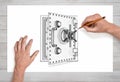 A pair of male hands in close view draws an open metal safe box with a pencil on white paper.