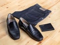 A pair of men\'s maccassin-style shoes next to jeans and a wallet against a light wooden surface Royalty Free Stock Photo