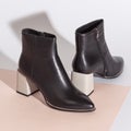 Pair of new black women short boots on medium high heels on beige background studio shot