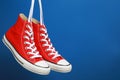 Pair of new stylish red sneakers hanging on laces against blue background. Space for text Royalty Free Stock Photo