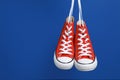 Pair of new stylish red sneakers hanging on laces against blue background. Space for text Royalty Free Stock Photo