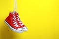 Pair of new stylish red sneakers hanging on laces against yellow background. Space for text Royalty Free Stock Photo