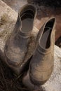 A pair of old dirty galoshes with water inside on stones