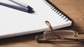 Pair of pens on a notebook with glasses on a wooden table at home