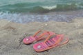 Pair of pink flip flops female shoes at sandy beach with sea waves view and shells Royalty Free Stock Photo