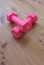 Pair of pink light weight dumbells in a crossed position on a light wood background, copy space