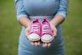 A pair of pink toddler sneakers in the hands of pregnant woman