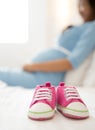 A pair of pink toddler sneakers beside a pregnant woman, focus o