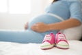 A pair of pink toddler sneakers beside a pregnant woman, focus o