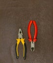 Pair of pliers red pens and black, yellow lies on a brown background