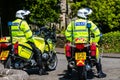 Pair police scotland motorcyclists parked up and astride their bikes looking down the road on a sunny day