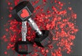Pair of 15-pound dumbbells on a black gym floor, shiny red confetti hearts, red sparkly heart