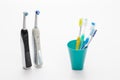 Pair of Professional Electric Toothbrushes In Front of Four Manual Tooth Brushes in One Cup On White Background