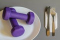 A pair of purple dumbbells in a white plate, fork and spoon on a napkin. concept of a healthy lifestyle
