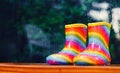 Pair of rainbow rain boots sitting outside with a rainy blurred out background