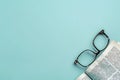 A pair of reading glasses rests on an open book, with the pages facing up and the book placed on a light blue background Royalty Free Stock Photo