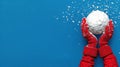 A pair of red mittened hands hold a snowball against a bright blue background, with a sprinkle of snowflakes