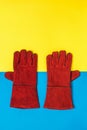 A pair of red welder`s gloves on a yellow and blue background. Royalty Free Stock Photo
