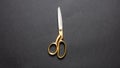 Pair of scissors gold handle isolated on black background, top view