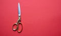 Pair of scissors gold handle isolated on red background, top view