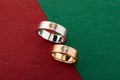 Pair of silver mens ring and pink gold womens ring decorated with tree on contrast green and red background Royalty Free Stock Photo