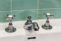 A pair of silver taps on a white sink and green tiles in the bathroom