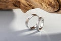Pair of silver wedding rings with diamonds on gray background with wood