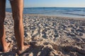 A pair of skinny male hairy legs in summer on the sandy beach in front of the blue sea