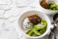 A pair of small dessert bowls with fresh kiwi fruit, white ice cream, yogurt and chocolate chips on a white stone background