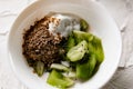 A pair of small dessert bowls with fresh kiwi fruit, white ice cream, yogurt and chocolate chips on a white stone background