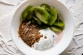 A pair of small dessert bowls with fresh kiwi fruit, white ice cream, yogurt and chocolate chips on a white stone background