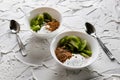 A pair of small dessert bowls with fresh kiwi fruit, white ice cream, yogurt and chocolate chips on a white stone background