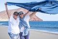 A pair of smiling and cheerful sisters enjoying the winter sea on a windy day holding a scarf in the sea breeze. Active elderly