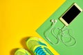 Pair of sport shoes and mobile cellphone with earphones on colorful background. New sneakers on green and yellow background.