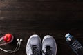 Pair sports shoes, headphones, apple and water bottle on black wood