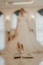 Pair of stylish bridal shoes with the blurry silhouette of the bride in the background.